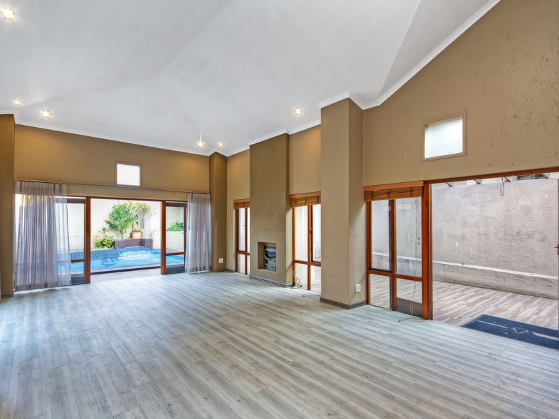 Spacious living area featuring vaulted ceilings, laminate flooring, a built-in fireplace, and large sliding glass doors providing seamless access to the outdoor pool area.