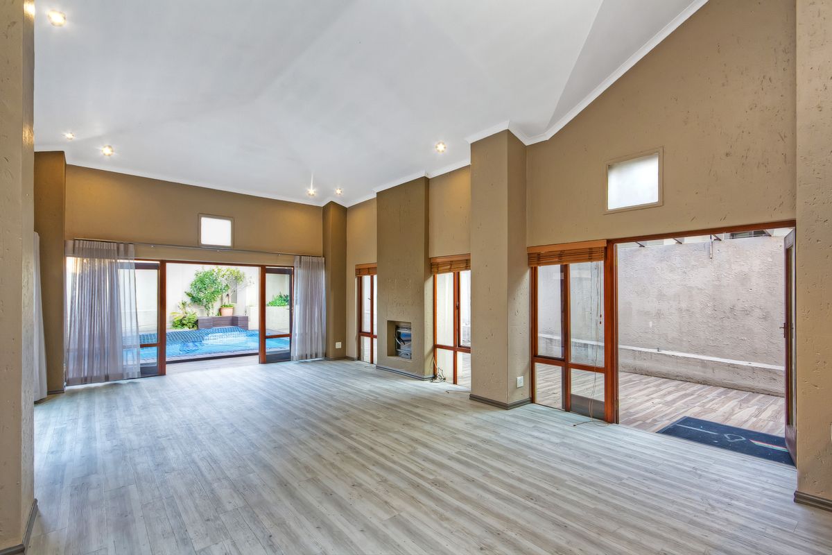 Spacious living area featuring vaulted ceilings, laminate flooring, a built-in fireplace, and large sliding glass doors providing seamless access to the outdoor pool area.