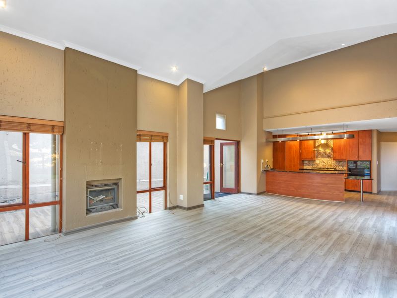 Spacious open-plan living area featuring high ceilings, laminate flooring, a built-in fireplace, and an integrated kitchen with wooden cabinetry.
