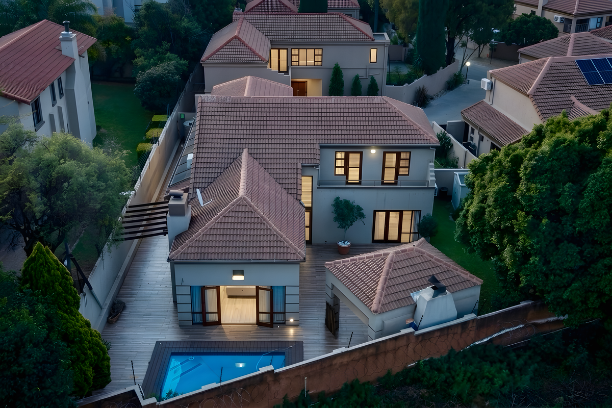 Aerial view of a residential property featuring a tiled roof, swimming pool, timber decking, and an outdoor fireplace in a landscaped garden setting.