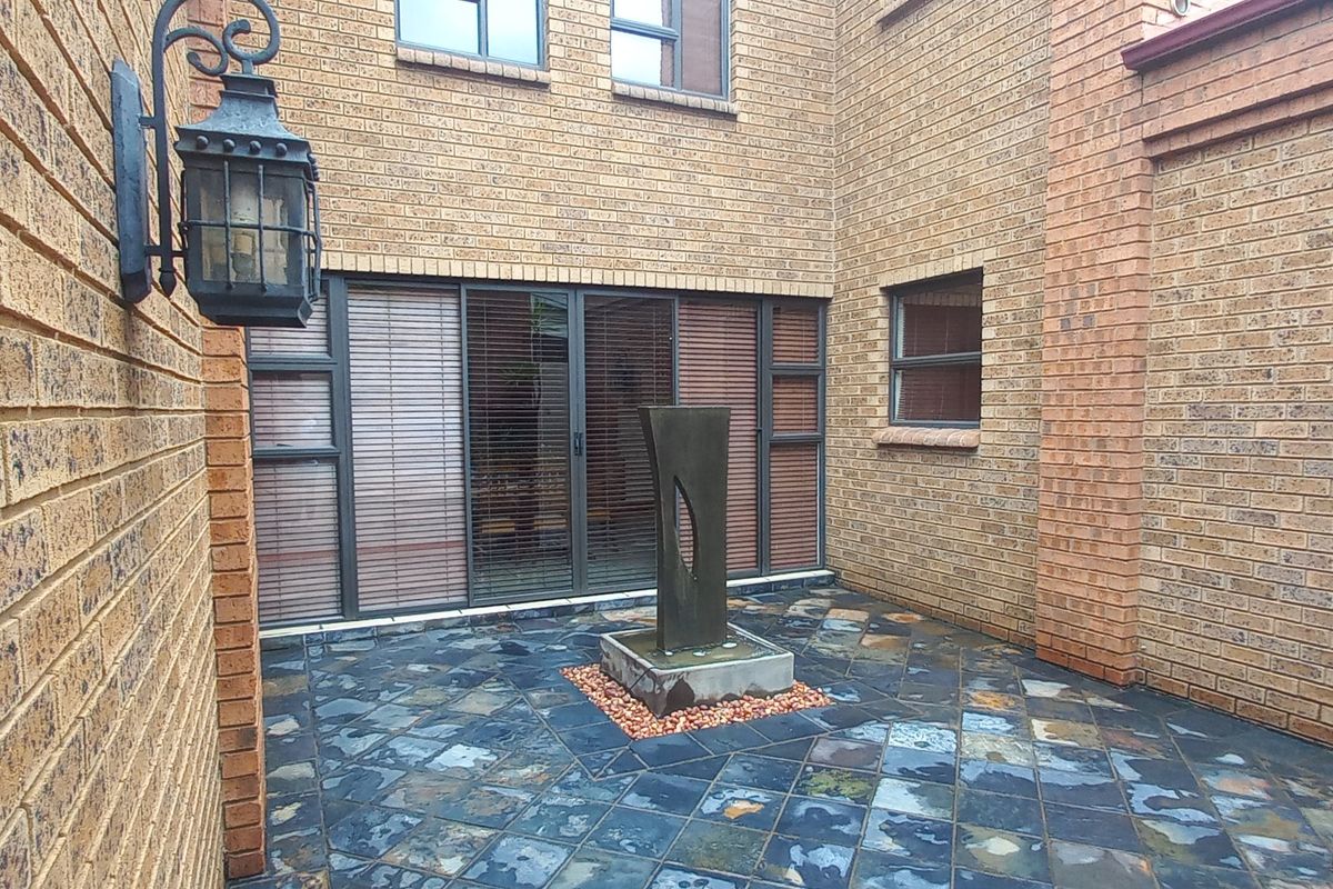 A private rear courtyard featuring face brick walls, slate tile flooring, and a central water feature, providing a quiet outdoor space.