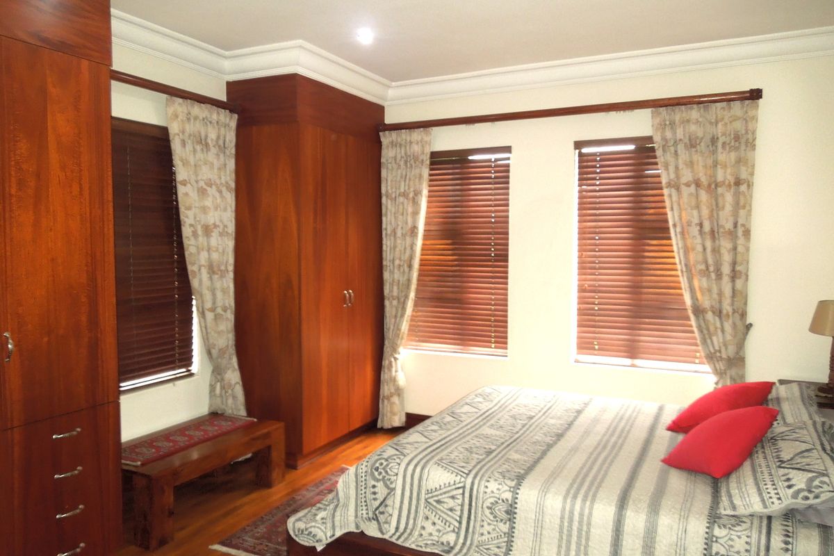 A well-maintained bedroom featuring warm wooden flooring, extensive built-in cabinetry, crown molding, and natural light filtered through wooden venetian blinds.