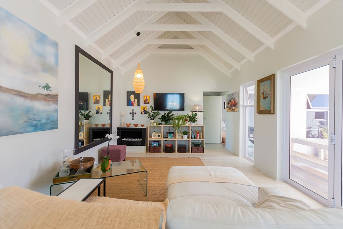 Bright living room featuring a high vaulted ceiling with exposed white beams, a built-in fireplace, and large glass sliding doors leading outdoors.