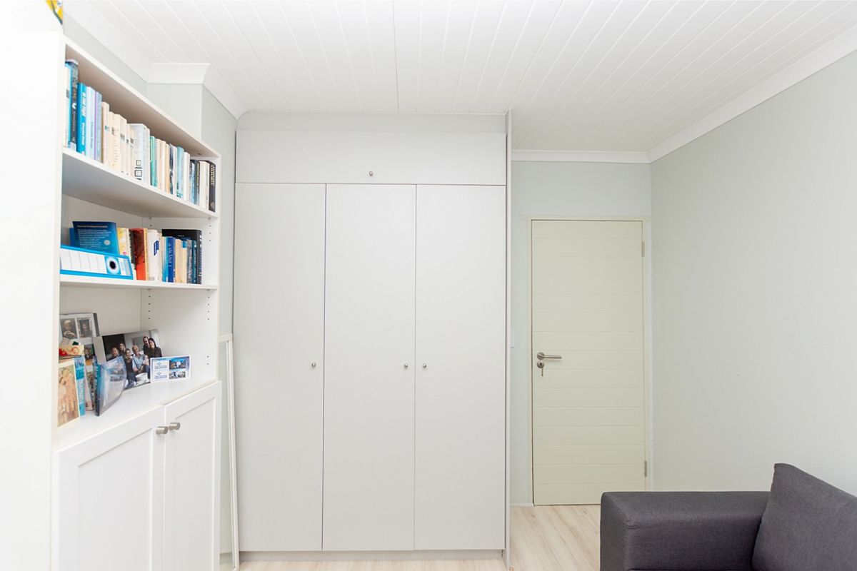 A clean bedroom featuring built-in cupboards, integrated shelving, and a white tongue and groove ceiling with matching cornice.