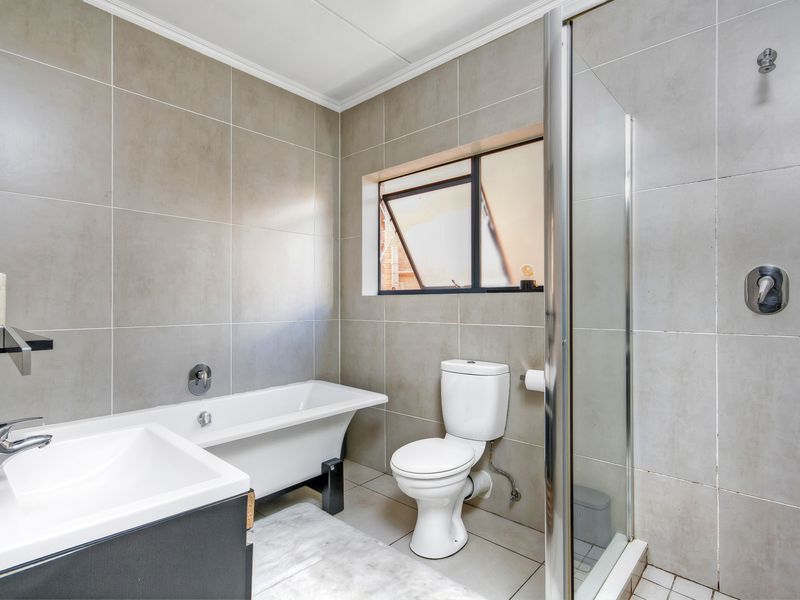 Modern bathroom featuring a freestanding bathtub, separate glass-enclosed shower, vanity basin, and neutral floor-to-ceiling tiling.