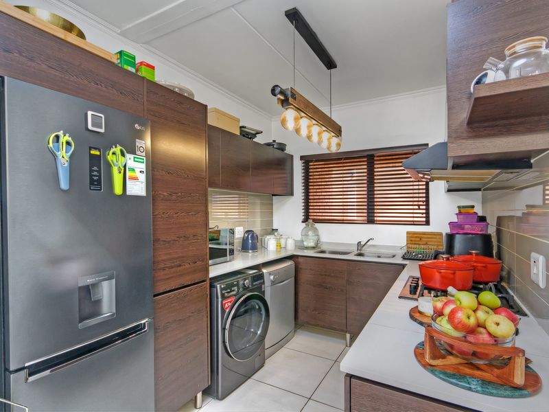 A well-maintained kitchen featuring dark wood cabinetry, a gas hob with extractor fan, double sink, and tiled flooring.