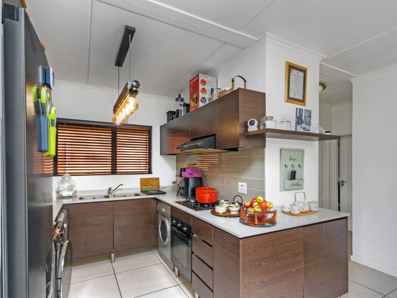 A compact, modern kitchen featuring dark wood cabinetry, a tiled backsplash, integrated oven and hob, and a stainless steel sink.
