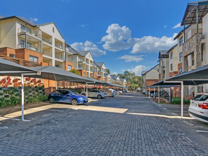 Exterior view of an apartment complex featuring paved driveway, covered parking bays with shade cloth, and multi-story residential buildings with balconies.