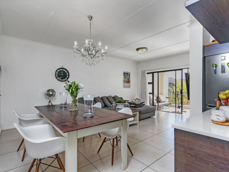 An open-plan living and dining area featuring tiled flooring, a modern chandelier, and a sliding glass door leading to a balcony.