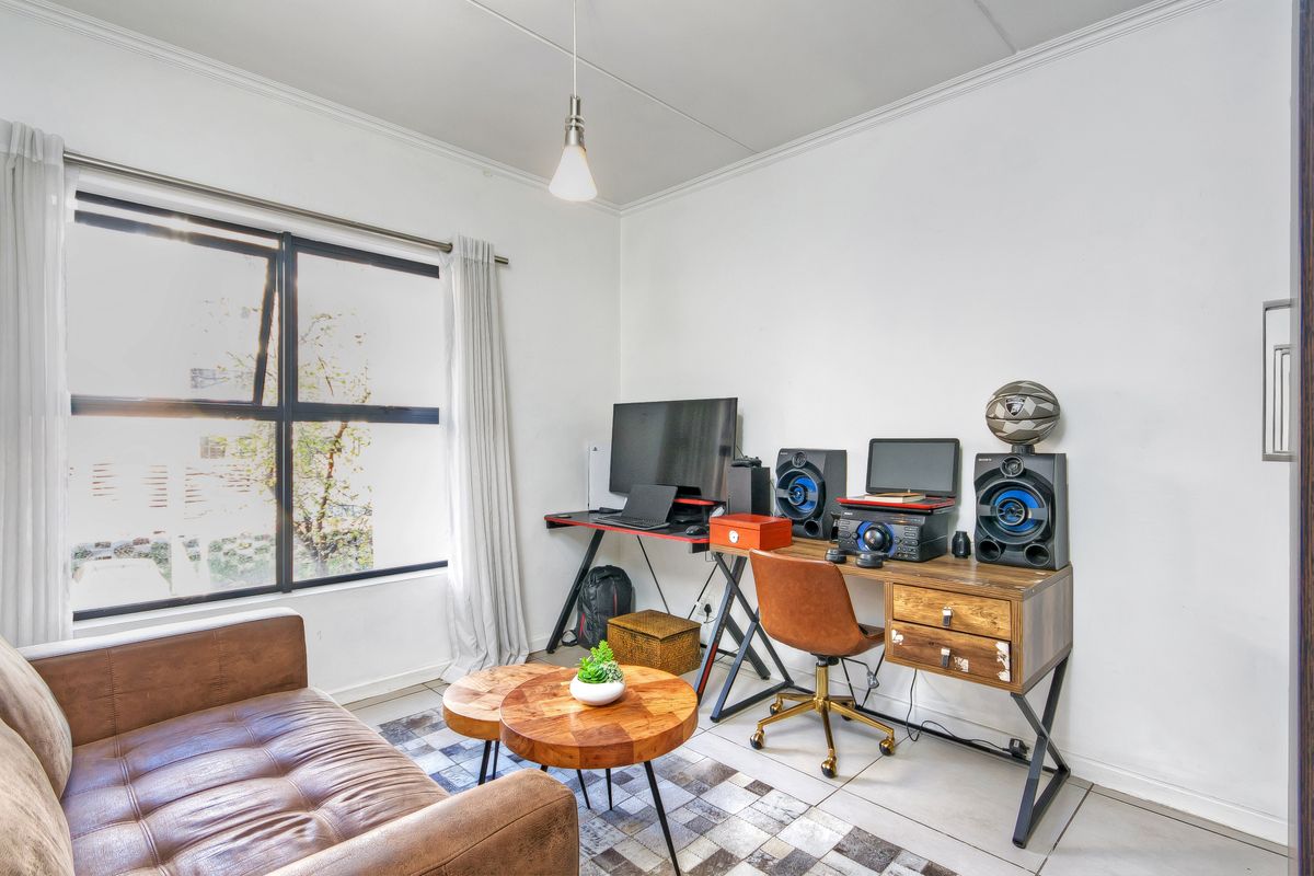 A bright living room featuring tiled flooring, a large window providing natural light, and a coved ceiling with a modern pendant light fixture.