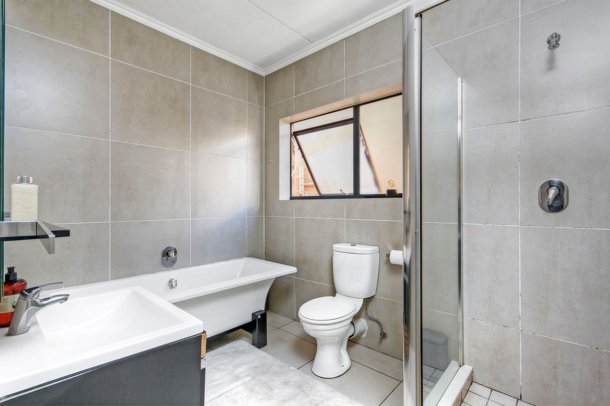 Modern bathroom featuring a freestanding bathtub, separate glass-enclosed shower, vanity basin, and neutral floor-to-ceiling tiling.