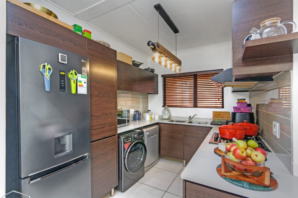 A well-maintained kitchen featuring dark wood cabinetry, a gas hob with extractor fan, double sink, and tiled flooring.