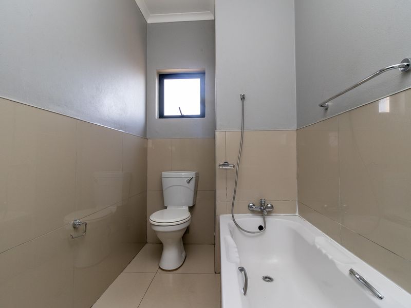 A functional bathroom featuring a bathtub with a handheld shower mixer, a toilet, and neutral wall and floor tiling.