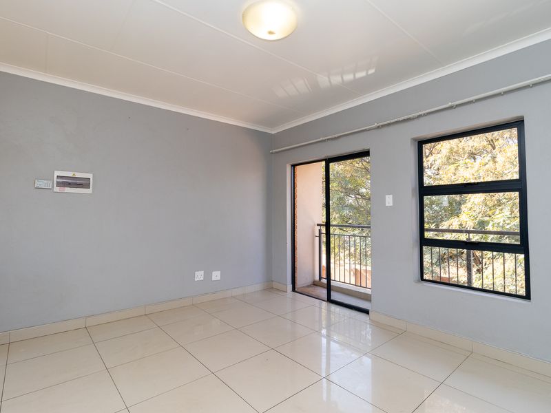 A bright, empty living area featuring neutral grey walls, large tiled floors, and a sliding door leading to a private balcony.