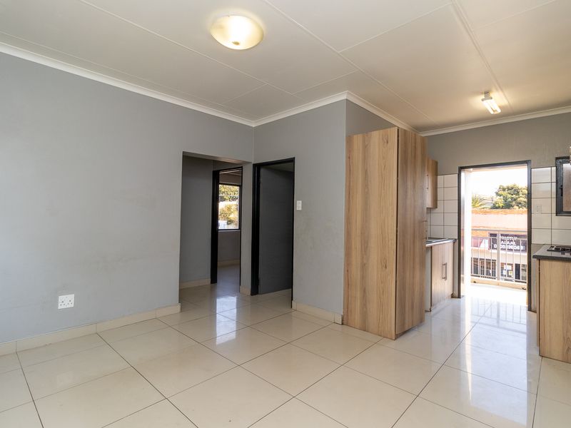 An open-plan living and kitchen area featuring tiled flooring, modern wood-finish cabinetry, and direct access to an outdoor balcony.