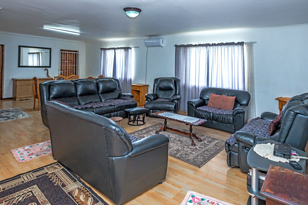 Spacious living room featuring light wood-look flooring, wall-mounted air conditioning unit, and large windows with curtains.