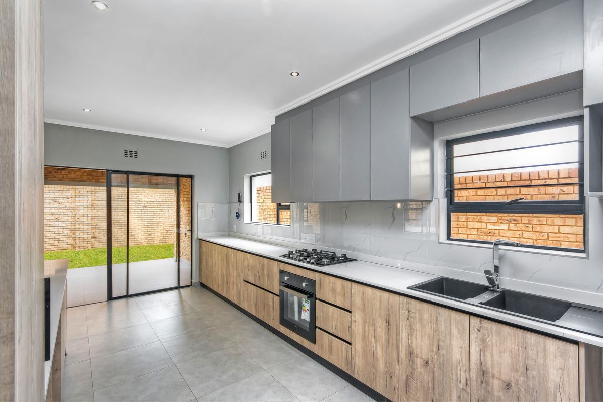 Modern kitchen featuring sleek two-tone cabinetry, stone countertops, integrated gas hob and oven, double sink, and direct access to the rear patio.