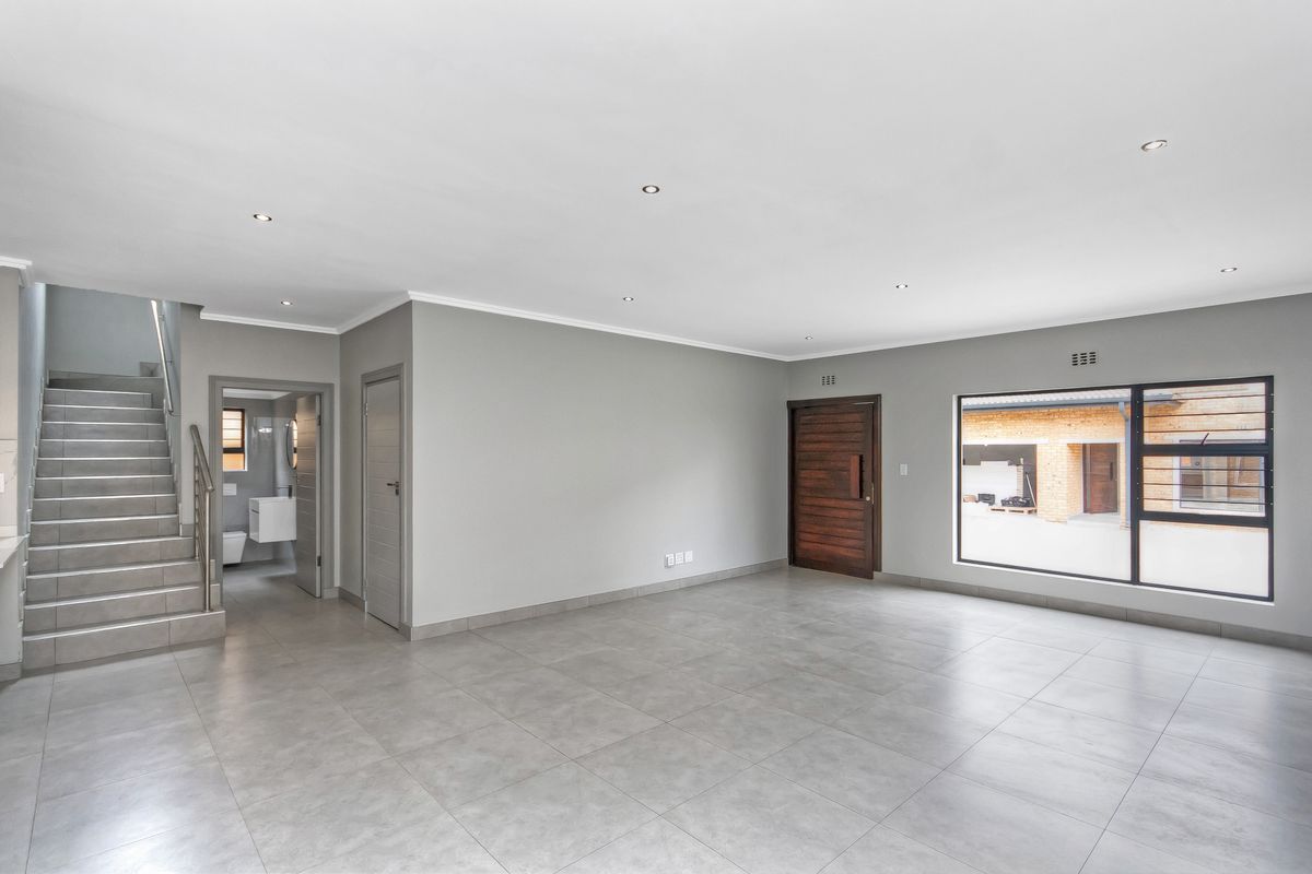 Spacious, modern open-plan living area featuring neutral tiled flooring, recessed downlights, and a contemporary staircase leading to the upper level.