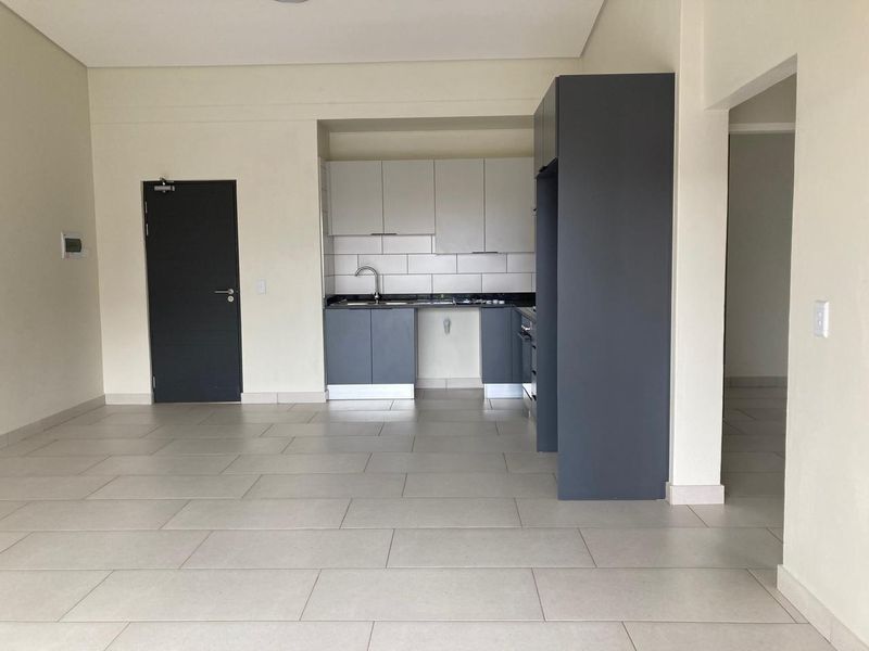 A modern, empty kitchen featuring two-tone cabinetry, stone countertops, a stainless steel sink, and neutral tiled flooring in an open-plan layout.