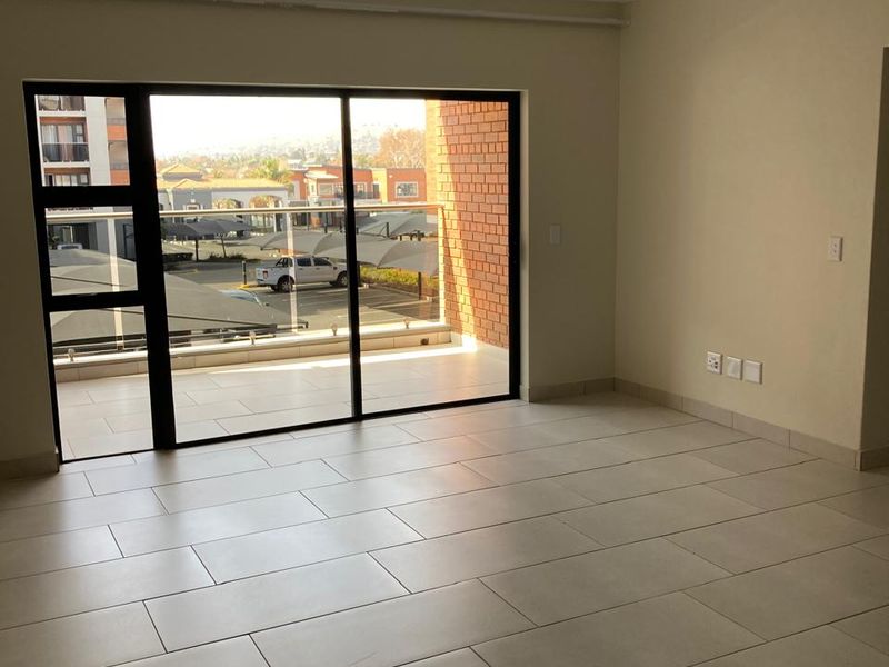 A bright, empty living area featuring neutral tiled flooring and a large sliding glass door that opens onto a private balcony.