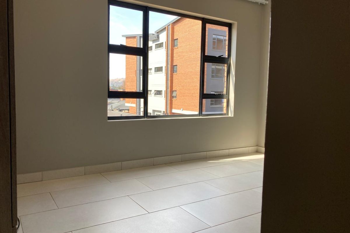 A bright, empty bedroom featuring neutral tiled flooring and large aluminium-framed windows, offering a clean and modern blank canvas.
