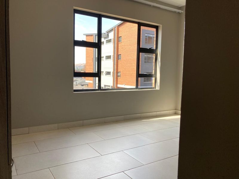 A bright, empty bedroom featuring neutral tiled flooring and large aluminium-framed windows, offering a clean and modern blank canvas.