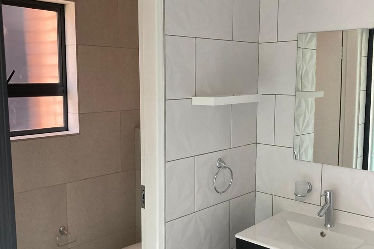 Modern bathroom featuring a wall-mounted vanity with basin, tiled walls, and a separate toilet area with neutral finishes.