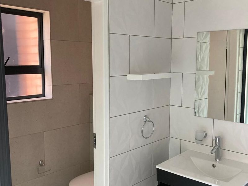 Modern bathroom featuring a wall-mounted vanity with basin, tiled walls, and a separate toilet area with neutral finishes.