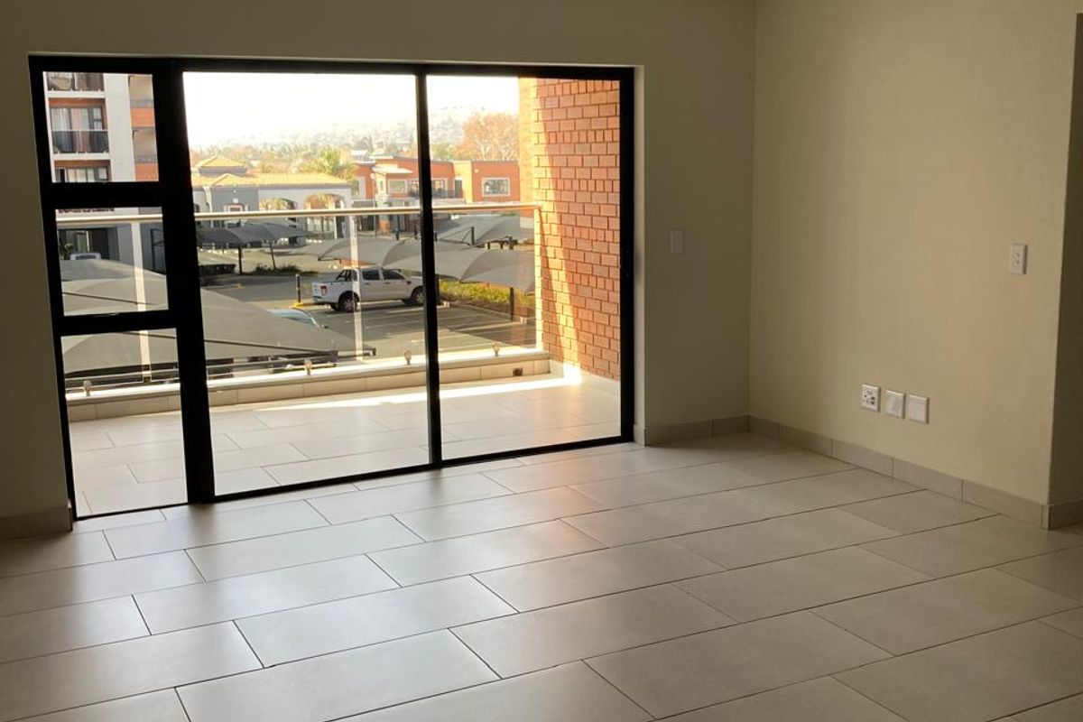 A bright, empty living area featuring neutral tiled flooring and a large sliding glass door that opens onto a private balcony.