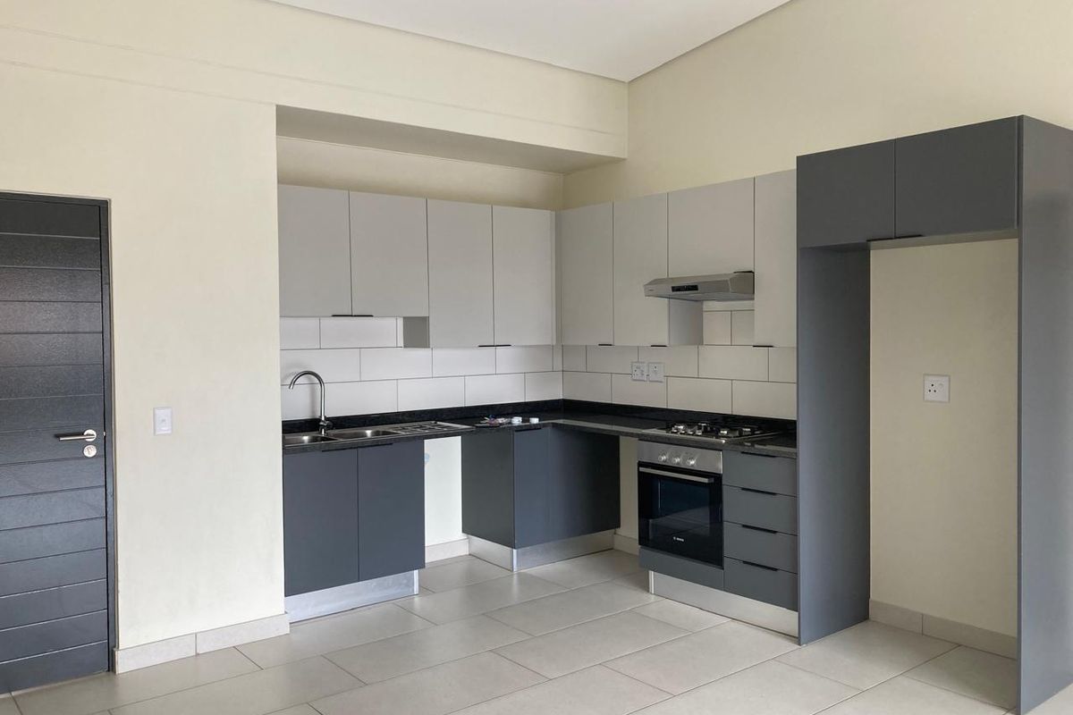 Modern kitchen featuring sleek two-tone cabinetry, granite countertops, built-in oven, gas hob, and extractor fan, finished with neutral floor tiles.