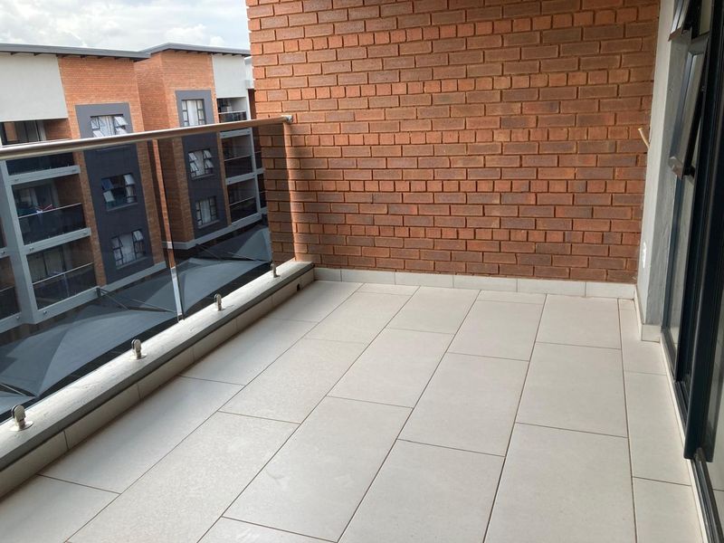 A clean, modern balcony featuring a glass balustrade, stainless steel railing, and exposed brick wall, offering a bright and open outdoor space.