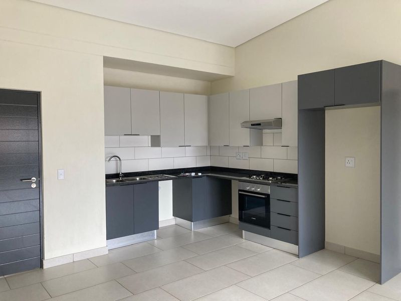Modern kitchen featuring sleek two-tone cabinetry, granite countertops, built-in oven, gas hob, and extractor fan, finished with neutral floor tiles.