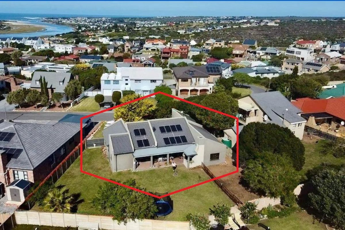 Aerial view of a residential property featuring a metal roof with solar panels, a covered patio, and a spacious fenced garden in a coastal suburb.