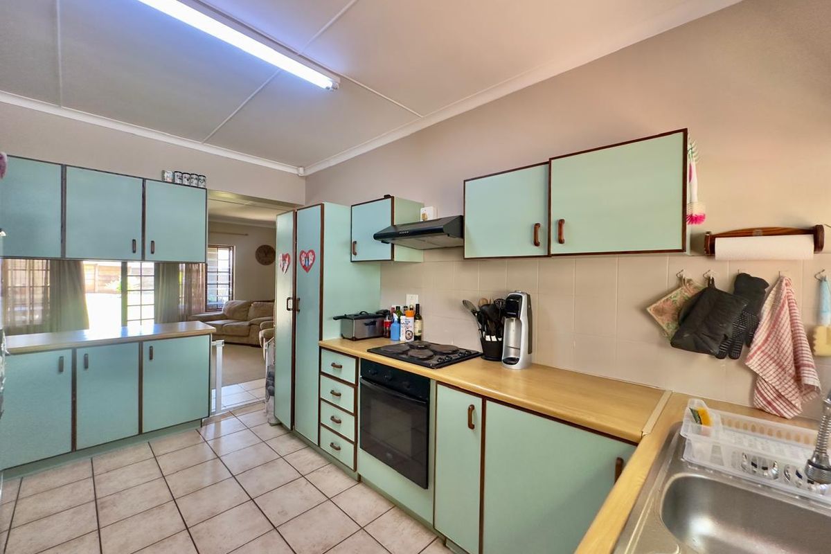 A functional kitchen featuring light green cabinetry, laminate countertops, built-in oven with gas hob, and tiled flooring, offering a classic layout with ample storage.