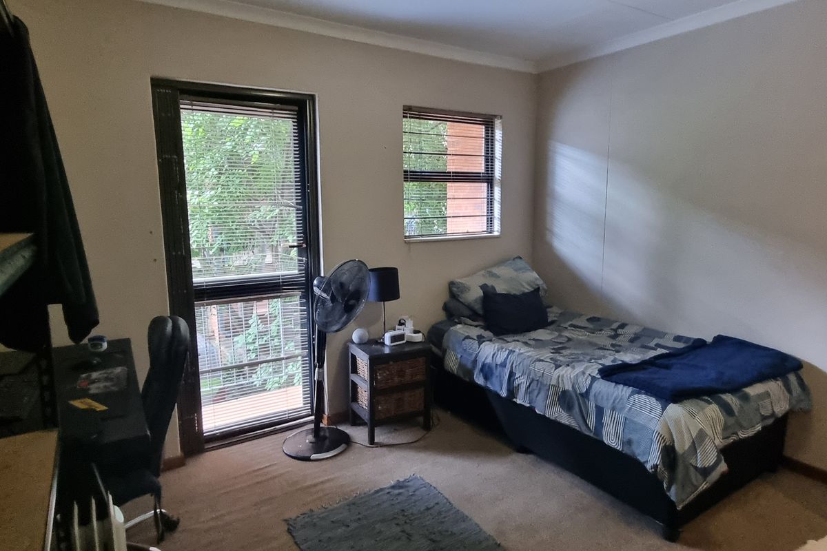 A standard bedroom featuring carpeted flooring, aluminium window frames with security bars, and direct access to an outdoor balcony area.
