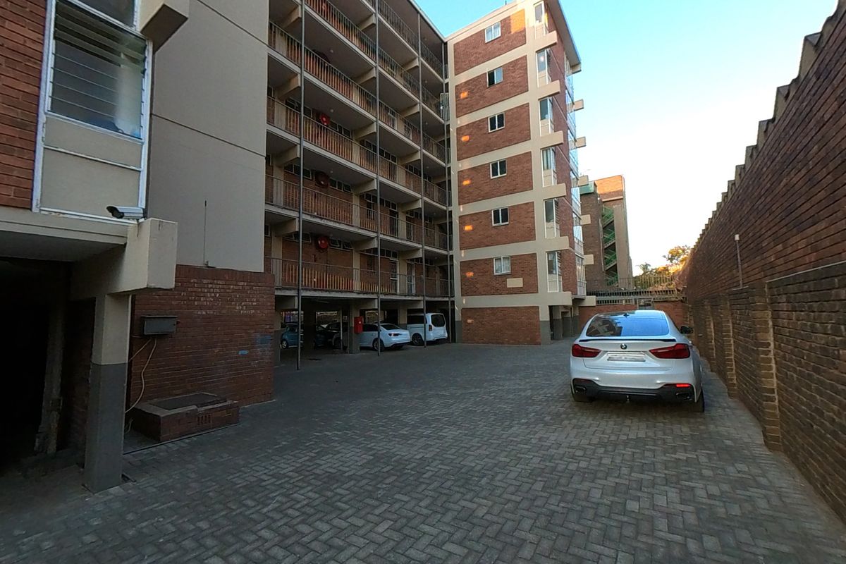 Rear exterior view of a multi-story apartment building featuring brick facade, paved parking area, and balcony access.