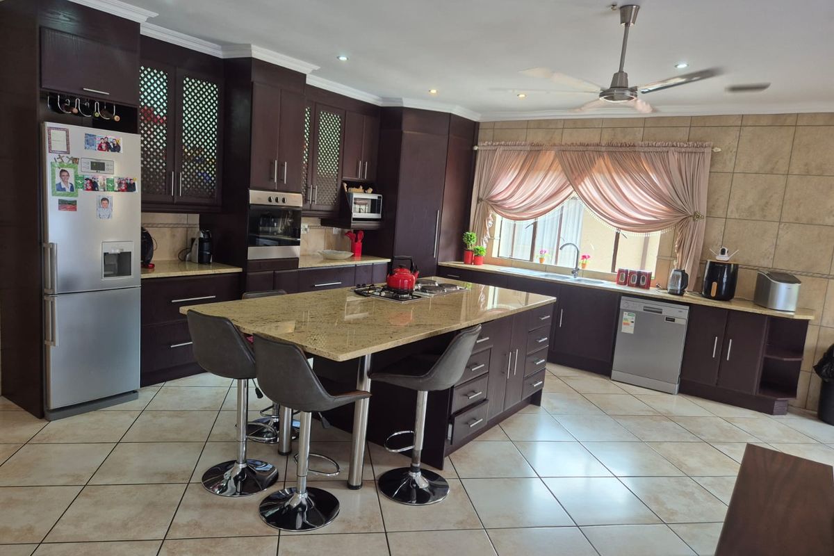 Spacious kitchen featuring dark wood cabinetry, granite countertops, a central island with a gas hob, and tiled flooring throughout.