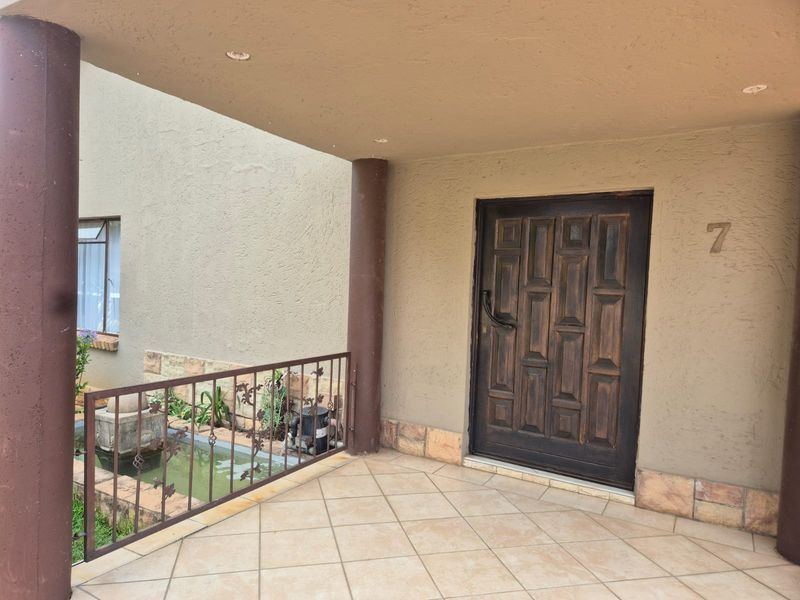 Covered front entrance porch featuring tiled flooring, stone cladding accents, and a solid wood front door with wrought iron railing.