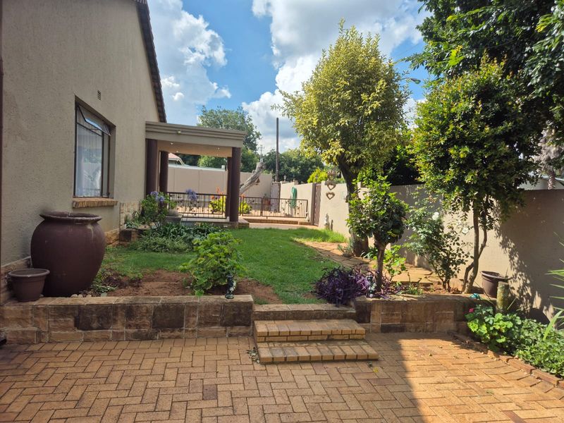 A well-maintained rear garden featuring a brick-paved patio, tiered retaining walls with steps, and a covered outdoor entertainment area.