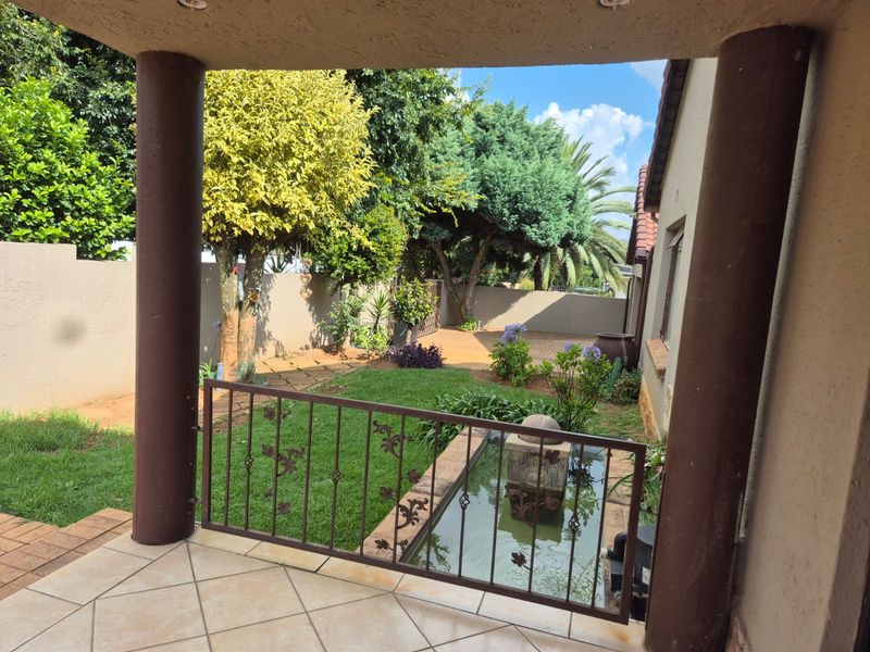 A covered patio overlooking a landscaped garden featuring a built-in water feature, lush lawn, and secure boundary walls.