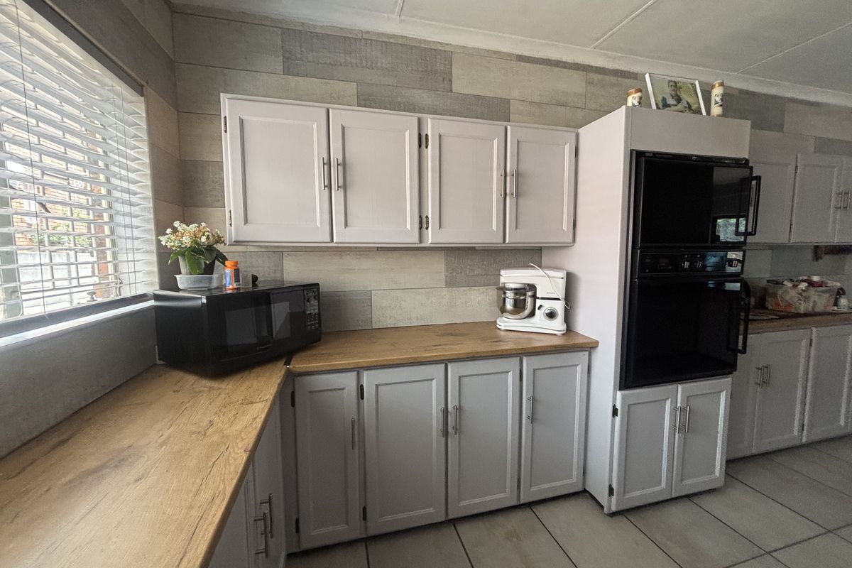 A functional kitchen featuring light grey cabinetry, wood-look laminate countertops, built-in double oven, and tiled flooring with natural light from the window.