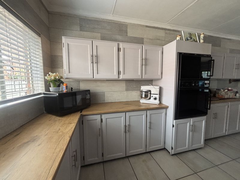 A functional kitchen featuring light grey cabinetry, wood-look laminate countertops, built-in double oven, and tiled flooring with natural light from the window.
