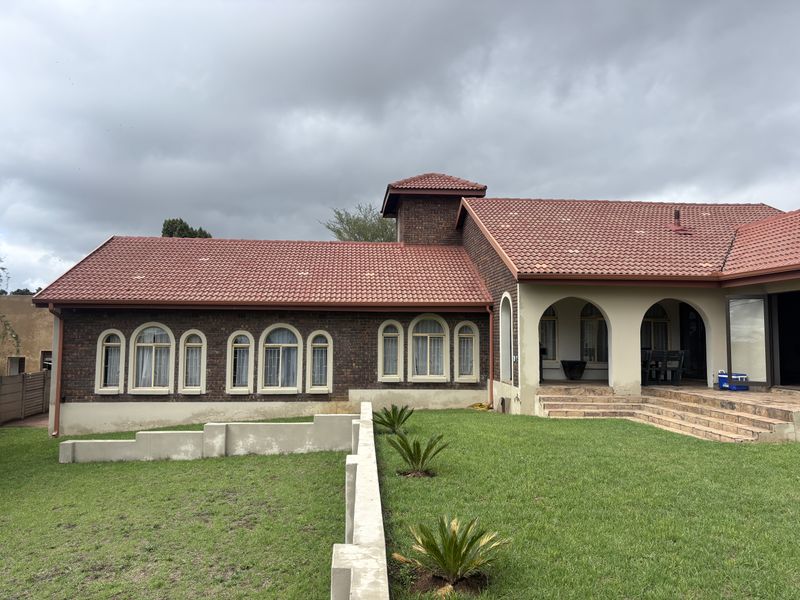 Rear view of a brick house featuring a tiled roof, arched windows, and a covered patio area overlooking a landscaped garden.