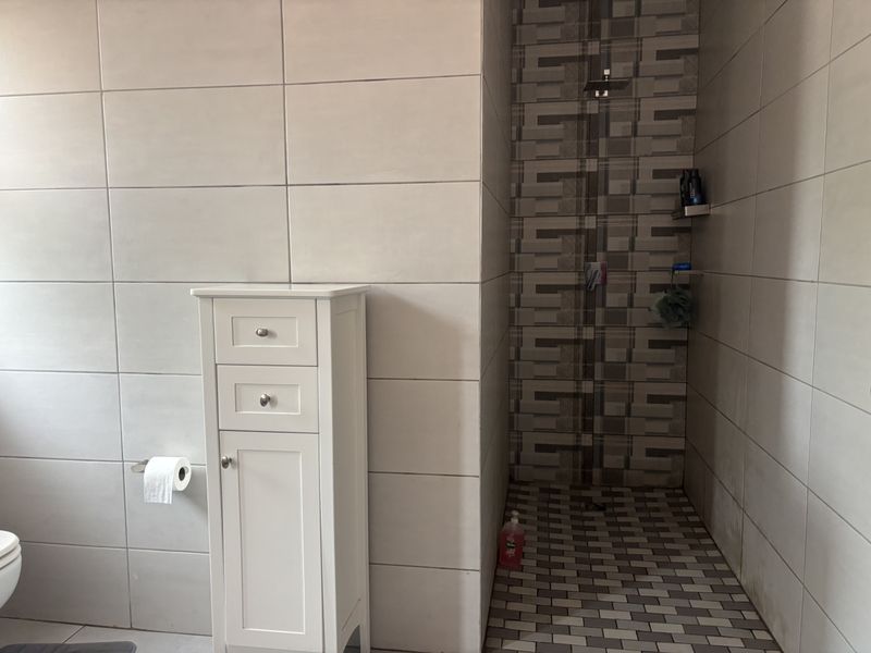 A modern bathroom featuring a walk-in shower with a rainfall shower head, decorative tiled accents, and neutral wall tiling.