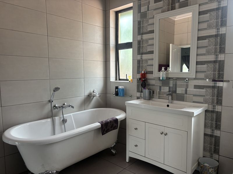 A well-maintained bathroom featuring a classic freestanding bathtub, a modern vanity with basin, and stylish patterned wall tiling.