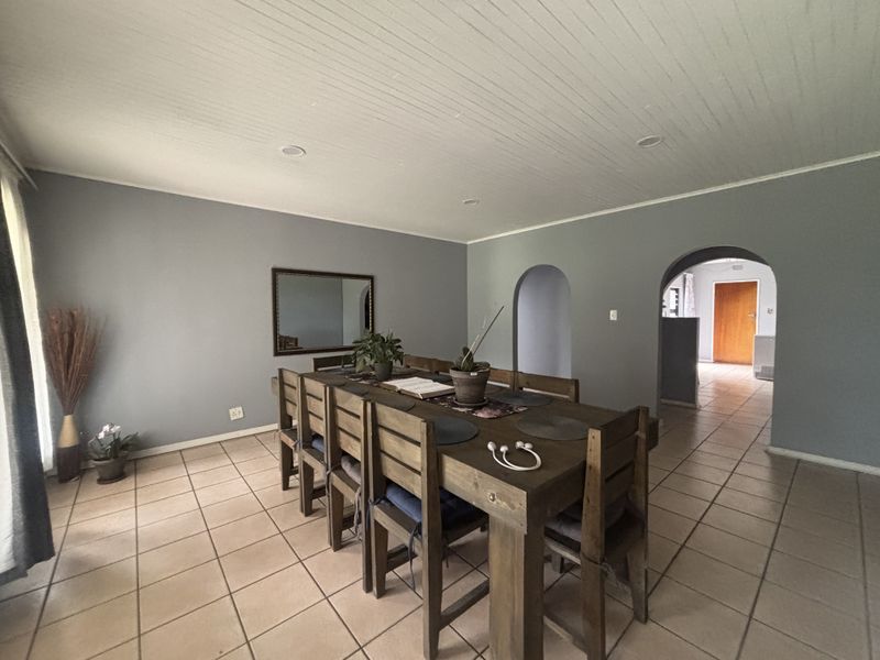 A spacious dining room featuring tiled flooring, arched architectural doorways, and a classic tongue and groove ceiling with recessed lighting.
