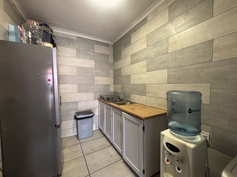 A functional scullery area featuring a stainless steel sink, wooden countertop, built-in cabinetry, and modern tiled wall finishes.