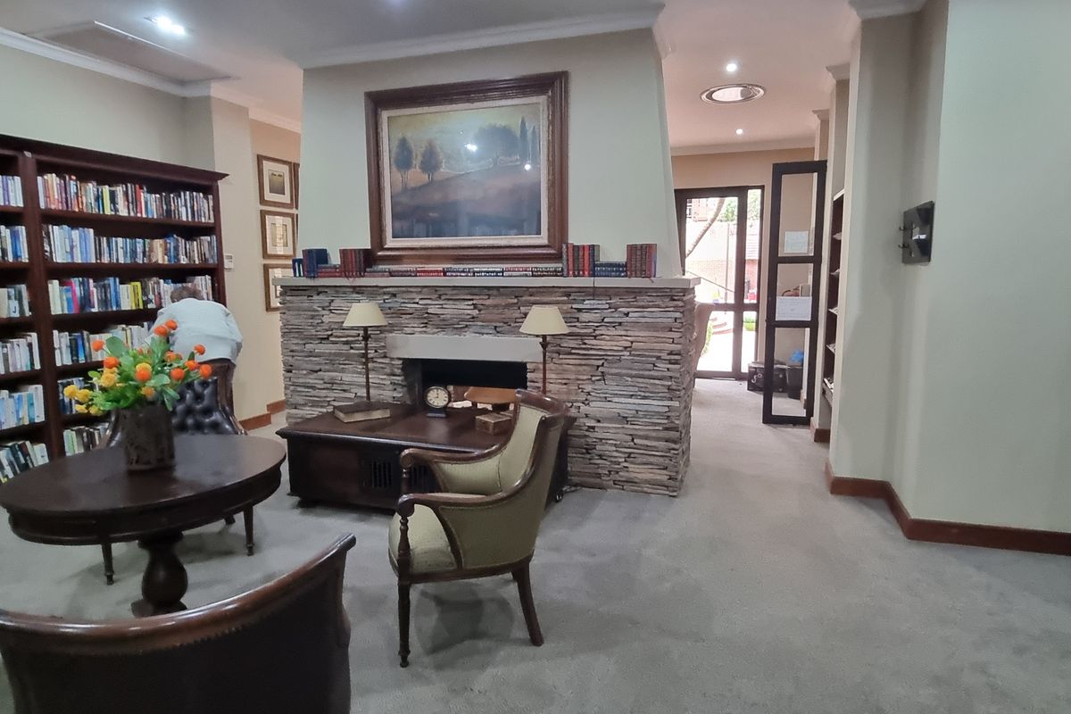 A cozy communal library or lounge area featuring a prominent stone-clad fireplace, extensive built-in shelving, and recessed lighting.