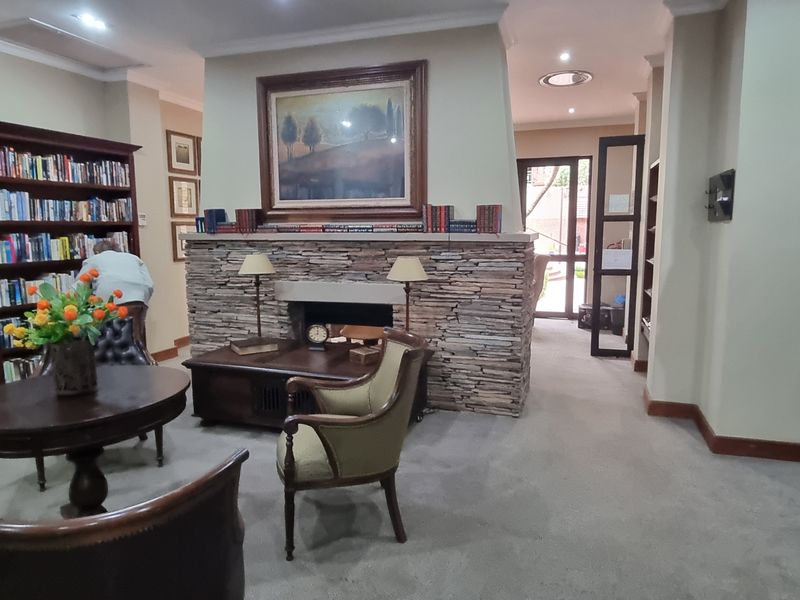 A cozy communal library or lounge area featuring a prominent stone-clad fireplace, extensive built-in shelving, and recessed lighting.