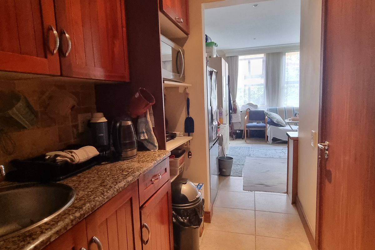 A compact kitchen featuring wooden cabinetry, granite countertops, and a stainless steel sink, leading into an adjacent living area.